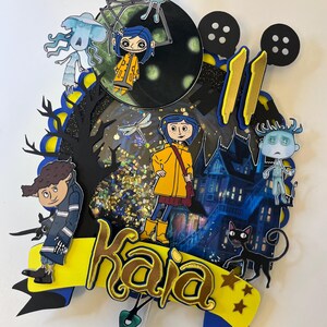 May include: A layered cake topper featuring characters from the animated film "Coraline." The design includes a yellow banner with the name "Kaja," a haunted house, black cat, and various character cutouts. The number "11" is also included.