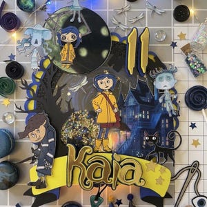 May include: A colorful cake topper featuring characters from the animated film "Coraline." The design includes a central image of the character, the name "Kaia," and the number "11." Decorative elements include buttons, keys, and miniature bottles.