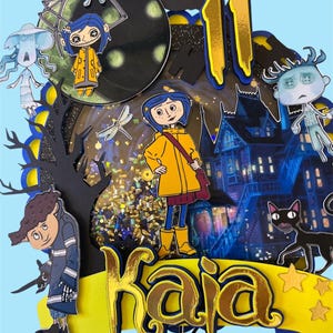 May include: A layered, colorful cake topper featuring characters and elements from the animated film "Coraline." The design includes the name "Kaia" in gold lettering, the number "11," and various character cutouts, all set against a blue background.