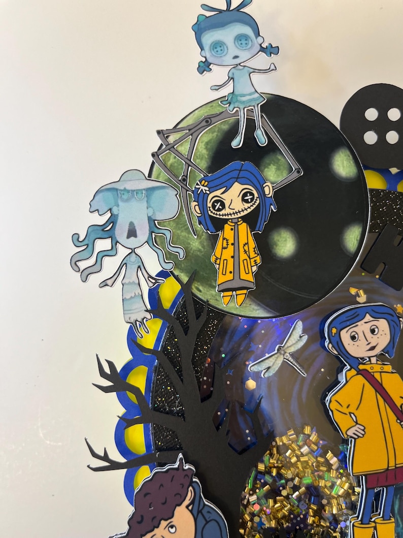 May include: A colorful, layered artwork featuring characters from the animated film "Coraline." The design includes cut-out figures, a dark tree silhouette, a large button, and a glittery, textured element. The color palette includes blue, yellow, and black.