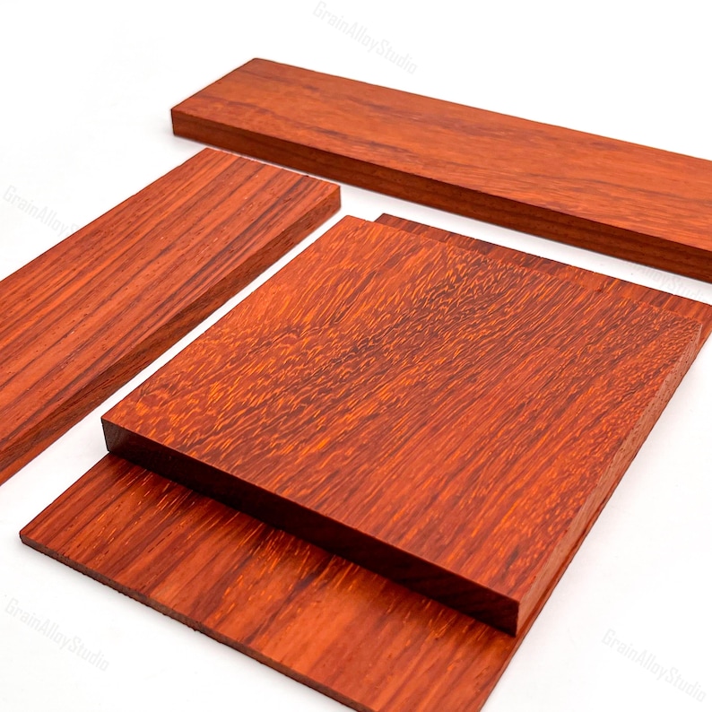 May include: Three rectangular pieces of reddish-brown wood with a visible grain pattern. The pieces are arranged in a layered composition, featuring one long narrow board, one medium rectangular board, and one large square board.