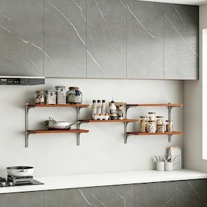 May include: A set of wall-mounted wooden shelves with metal brackets, featuring various glass storage jars, a small frying pan, spice bottles, and a ceramic egg holder. The shelves are positioned below grey marble-patterned kitchen cabinets.