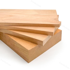 Puede incluir: Una pila de tablas de madera sin terminar, de color marrón claro. La veta de la madera es visible en la superficie de cada pieza. Las tablas son rectangulares y varían ligeramente en tamaño, con un tono natural y cálido.