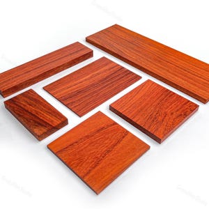 May include: A collection of six rectangular wooden boards with a rich reddish-brown hue and visible natural grain patterns. The pieces vary in size and are arranged in a scattered formation, showcasing smooth, flat surfaces and clean, sharp edges.