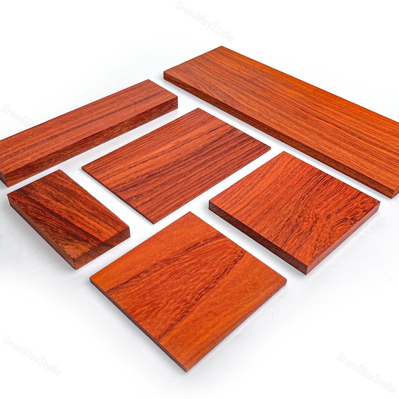 May include: A collection of six rectangular wooden boards with a rich reddish-brown hue and visible natural grain patterns. The pieces vary in size and are arranged in a scattered formation, showcasing smooth, flat surfaces and clean, sharp edges.