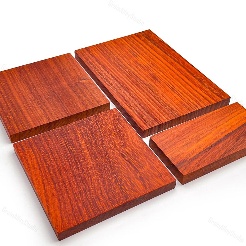 May include: Four rectangular blocks of reddish-brown wood with visible grain patterns. The pieces are arranged in a cluster, showcasing smooth, flat surfaces and sharp, clean edges. Each block displays a distinct natural wood texture and deep color.