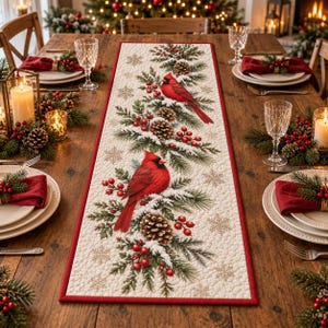 May include: A rectangular table runner featuring a cream-colored quilted fabric with a repeating pattern of two bright red cardinal birds perched on snow-dusted pine branches, pinecones, red berries, and gold-toned snowflake accents.