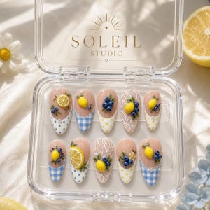 May include: A set of ten almond-shaped press-on nails in a clear plastic case labeled Soleil Studio. The nails feature a nude base with 3D lemon and blueberry accents, white lace patterns, and blue and white gingham or polka dot tip designs.