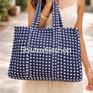 Può includere: Una borsa tote rettangolare con un motivo a scacchi blu scuro e bianco. La borsa è dotata di due robusti manici superiori e la scritta Shivtextileshop è stampata in bianco al centro del pannello frontale della borsa in tessuto.
