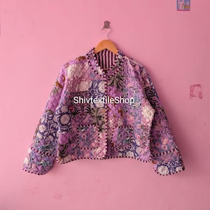 Può includere: Una giacca trapuntata con design patchwork in tonalità viola, lavanda e bianco con motivi floreali e botanici. La giacca presenta un colletto alla coreana, maniche lunghe, due tasche frontali e la scritta ShivtextileShop stampata in bianco.