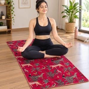Könnte beinhalten: Eine rechteckige Yogamatte mit leuchtend rotem Hintergrund und einem sich wiederholenden Muster aus tropischen Palmen, Geparden und Tukanen. Die Matte hat einen dekorativen genähten Rand und liegt auf einem hellen Holzboden.