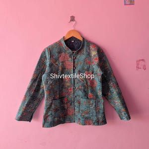 Peut inclure: Une veste matelassée bleu sarcelle avec un motif floral dans des tons de rouge, orange et bleu. La veste présente un col officier, des manches longues, deux poches plaquées à l'avant et quatre petits boutons ronds. Le texte ShivtextileShop est visible.