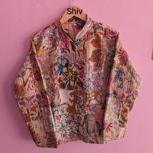 Può includere: Giacca trapuntata beige con un design patchwork floreale. La giacca presenta un colletto alla coreana e una chiusura con bottoni sul davanti. Il motivo floreale comprende fiori rosa, rossi e blu con foglie verdi. La parola "Shiv" è stampata sull'appendiabiti.