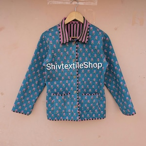 Könnte beinhalten: Eine gesteppte Jacke in Blaugrün mit einem sich wiederholenden rosa Blumenmuster, mit Kragen und Besatz in schwarz-rosa vertikalen Streifen. Die Jacke hat lange Ärmel, eine Knopfleiste und zwei Vordertaschen. Der Text ShivtextileShop ist sichtbar.