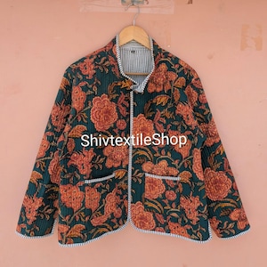 Könnte beinhalten: Eine gesteppte Jacke mit dunkelgrüner Basis und wiederkehrendem orangefarbenem Blumenmuster, langen Ärmeln, Stehkragen und zwei Vordertaschen. Die Kanten sind mit schwarz-weiß gestreiftem Stoff eingefasst. Der Text ShivtextileShop ist sichtbar.