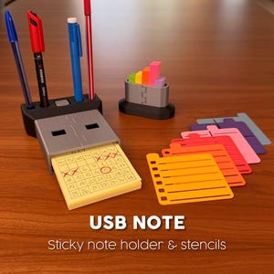 May include: A USB-shaped sticky note holder with a calendar, pens, and colourful stencils. The holder has a slot for a notepad and a pen holder. The stencils are in various colours, including orange, pink, and purple.