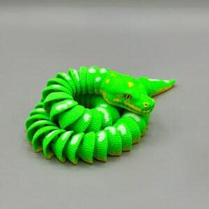 Peut inclure: Figurine de serpent vert enroul&eacute; avec des pois blancs et des d&eacute;tails jaunes. La t&ecirc;te du serpent est relev&eacute;e et ses yeux sont visibles. La figurine est faite d'un mat&eacute;riau c&ocirc;tel&eacute; et repose sur un fond gris.