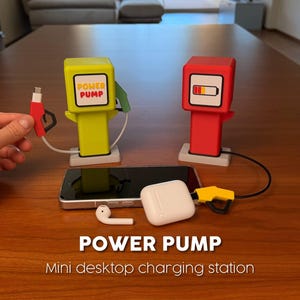 Pode incluir: Duas estações de carregamento de mesa em miniatura com formato de bombas de gasolina vintage, uma verde-limão e outra vermelha. A bomba verde tem uma etiqueta 'POWER PUMP', enquanto a vermelha exibe um ícone de bateria. Um bocal amarelo está ligado.