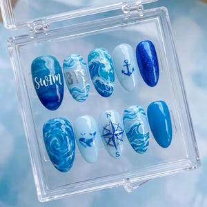 May include: A set of ten artificial nails in a clear plastic case. The nails feature various designs in shades of blue, including ocean waves, an anchor, a compass, and the text "SWIM BTS".