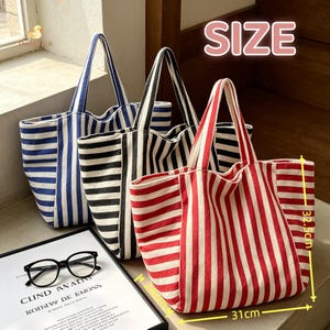 May include: Three canvas tote bags with vertical stripes in blue, black, and red. The bags feature two handles and a rectangular base. A yellow arrow diagram indicates dimensions of 32.5 cm in height and 31 cm in width. Black glasses are in the foreground.
