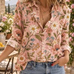 May include: A long-sleeved button-down shirt in a light pink hue featuring a repeating floral pattern of white daisies, pink poppies, and small blue flowers with green foliage. The shirt has a classic collar and is worn with blue denim jeans.