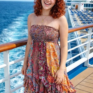 May include: A strapless, colorful patterned dress with a ruffled hem. The dress features a mix of floral and geometric designs in shades of pink, orange, and purple. The background shows a cruise ship and the ocean.