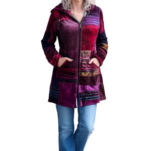 May include: A long, hooded velvet coat in shades of purple, burgundy, and black, with a full-length zipper and patch details. The coat is worn with blue jeans and white sneakers.