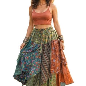 May include: A woman wearing a rust-colored crop top and a patchwork skirt. The skirt features panels of various patterns and colors, including floral, striped, and solid orange. The skirt is ankle-length and flowing.