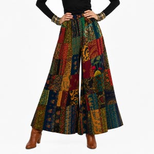May include: Wide-leg patchwork pants in a vibrant array of colors, including red, blue, green, and gold. The pants feature a high waist and a flared design, with a mix of patterned fabric patches. The model is wearing brown boots and a black long-sleeve shirt.