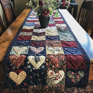 Può includere: Un runner da tavola trapuntato rettangolare caratterizzato da un design patchwork di vari quadrati di tessuto, ognuno contenente una forma a cuore cucita. I tessuti presentano motivi diversi, tra cui floreali, a quadri e tinte unite in rosso, blu e crema.