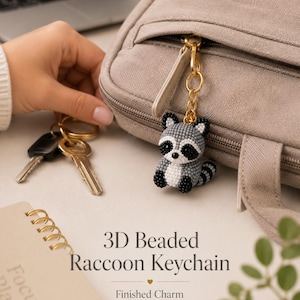 May include: A 3D beaded raccoon keychain featuring a small, round raccoon figure crafted from tiny grey, black, and white beads. The raccoon has a striped tail, black eye patches, and is attached to a gold-toned metal lobster clasp and ring.