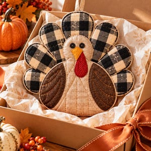 May include: A quilted turkey-shaped potholder featuring a black and white buffalo check pattern on the tail feathers, a tan textured body, brown wings, a yellow beak, and a red wattle, with two small black buttons serving as eyes.