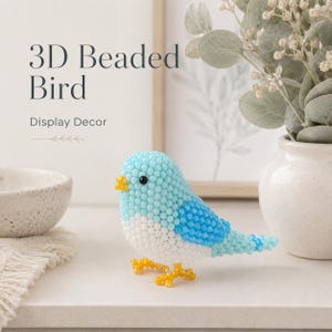 Könnte beinhalten: Eine 3D-Vogelfigur aus hellblauen, weißen und leuchtend blauen Perlen. Der Vogel hat einen kleinen gelben Schnabel, schwarze Perlenaugen und gelbe Perlenfüße. Der Text 3D Beaded Bird Display Decor ist in der oberen linken Ecke zu sehen.