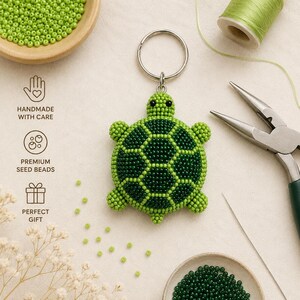 May include: A turtle-shaped keychain crafted from small lime green and dark forest green seed beads. The turtle features a round shell with a hexagonal pattern, a small head with two black bead eyes, and four stubby legs attached to a silver metal ring.