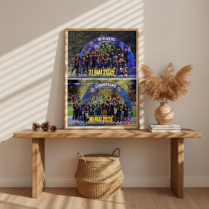 May include: A framed rectangular print featuring two stacked sports photographs of a football team celebrating under a blue archway. The top image displays the text WINNERS and 31 MAI 2025, while the bottom image displays CHAMPIONS and 30 MAI 2026 in yellow.