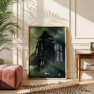 Peut inclure: Une affiche de film encadrée représentant une silhouette sombre et encapuchonnée en armure métallique au milieu d'une brume verte. Le texte en bas indique Marvel Studios, 12.18.26 et Avengers Doomsday, avec le logo Avengers en police moderne.