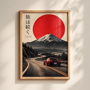 May include: A framed vertical wall art print featuring a red sports car driving on a winding road toward a snow-capped mountain under a large red sun. The Japanese text 旅は続く and the English text THE JOURNEY NEVER ENDS are printed on the left.