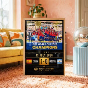 Peut inclure: Une affiche commémorative encadrée montrant une équipe de football célébrant sur un podium. Le texte indique FIFA WORLD CUP 2026 CHAMPIONS, FINAL 19 JULY 2026, SPAIN 1-0 ARGENTINA, et METLIFE STADIUM NEW JERSEY, USA, avec les drapeaux nationaux.