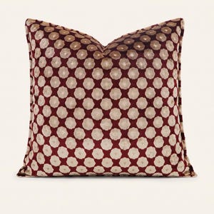 Könnte beinhalten: Ein quadratisches Kissen mit einer Basis aus tiefburgunderfarbenem Samt und einem sich wiederholenden Muster aus hellbeigen, kreisförmigen Blumenmotiven. Das Kissen hat eine weiche Textur und einen sauberen Keder am Rand.