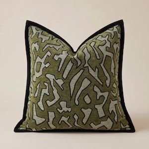 May include: Square decorative pillow with a green and white abstract pattern. The pillow has a black border. The pattern is a series of interconnected shapes. The pillow is a square shape.