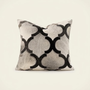 May include: A square throw pillow featuring a repeating quatrefoil pattern. The design consists of dark charcoal black and light grey textured hair-on-hide panels stitched together to create a geometric, high-contrast visual effect.
