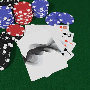 May include: A green felt poker table with stacks of red, blue, and black poker chips. A hand of cards is fanned out, showing the ten of hearts, diamonds, and spades. The cards have a black and white abstract design.