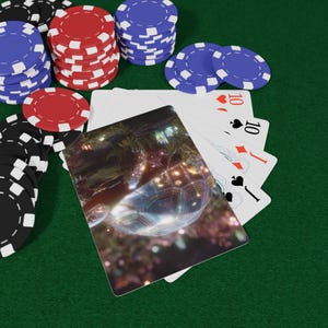 Puede incluir: Fichas de póquer negras, rojas y azules apiladas sobre una superficie de fieltro verde. Cartas de juego con el número 10 y una jota abanicadas. Una carta presenta una ilustración de tortuga.