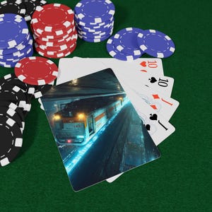 Puede incluir: Juego de póquer sobre una superficie de fieltro verde. Pilas de fichas de póquer rojas, negras y azules rodean una mano de cartas. Una carta presenta un tren en un túnel.