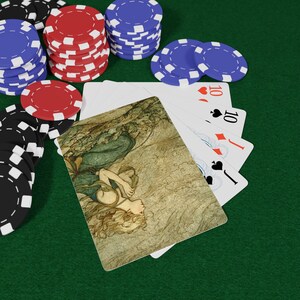 Puede incluir: Fichas de póquer negras, rojas y azules apiladas sobre una superficie de fieltro verde. Cartas de juego, incluido el número 10, y una ilustración decorativa están abanicadas. La imagen sugiere un juego de póquer o un tema de casino.