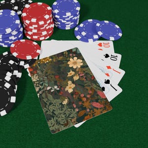 Puede incluir: Un juego de póquer con pilas de fichas rojas, azules y negras. Un mazo de cartas está extendido, con un diseño floral en el reverso de una carta. Las cartas muestran el número 10 y los palos de corazones, diamantes y picas.