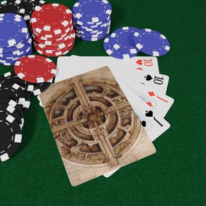 May include: Poker chips in red, black, and blue are stacked on a green felt surface. A deck of cards includes a card with a detailed architectural design and three cards showing the number 10.