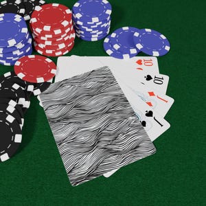 Puede incluir: Escena de juego de póquer con cartas que muestran el número 10 y una baraja con un diseño ondulado en blanco y negro. Montones de fichas de póquer rojas, azules y negras están sobre una superficie de fieltro verde.