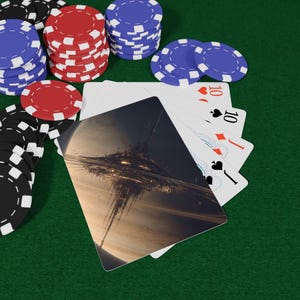 May include: Poker set on a green felt surface. Stacks of red, blue, and black poker chips surround a hand of playing cards. The cards show a futuristic space scene and the number 10 in hearts, spades, and diamonds.