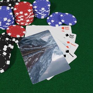 Puede incluir: Escena de póquer con cartas y fichas. Las cartas muestran un paisaje montañoso. Montones de fichas rojas, azules y negras están sobre una superficie de fieltro verde. Las cartas muestran el número 10.